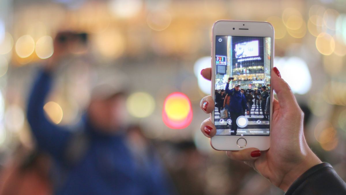 スマートフォンで渋谷のスクランブル交差点を撮る旅行者の手元